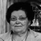 Retrato a preto e branco de uma mulher idosa, de frente para a câmara. Usa óculos e tem cabelo escuro.