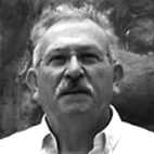 Retrato a preto e branco de um homem de cabelo grisalho e bigode, com uma camisola clara.