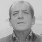 Retrato a preto e branco de um homem de meia-idade, enquadrado dos ombros para cima. Olha ligeiramente para cima.