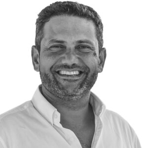 Retrato a preto e branco de um homem sorridente, com cabelo curto e barba, vestido com uma camisola clara. O fundo é branco e não há texto visível que permita identificá-lo.