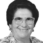Retrato a preto e branco de uma pessoa sorridente, com óculos e cabelo curto escuro. É visível uma peça de roupa com padrão.