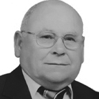 Retrato a preto e branco de um homem de fato e gravata, com óculos e pouco cabelo. O fundo é branco.