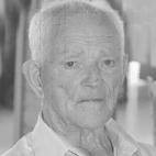 Retrato a preto e branco de um homem idoso, de cabelo branco e camisola clara, a olhar para a câmara.