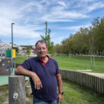Um homem posa num espaço verde, junto a um parque infantil. Ao fundo veem-se árvores e edifícios residenciais.