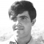 Retrato a preto e branco de um jovem, fotografado do peito para cima, com cabelo escuro e camisola clara. O fundo está desfocado.