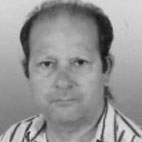 Fotografia de rosto, a preto e branco, de um homem a olhar para a câmara. Veste uma camisola às riscas.