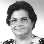 Retrato a preto e branco de uma mulher com óculos, cabelo curto e roupa estampada, sobre fundo claro.