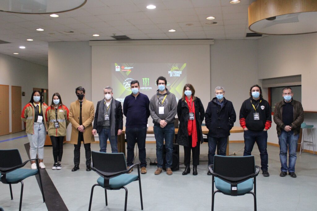 Nove pessoas com máscaras posam numa sala de conferências. Ao fundo, uma projeção mostra referências à Cruz Vermelha, à Monster Energy e ao Politécnico de Leiria.