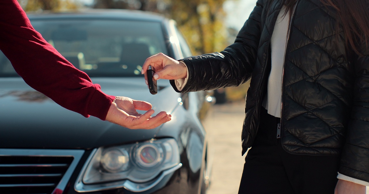 foto de um homem a entregar uma chave a uma mulher com um veículo em fundo