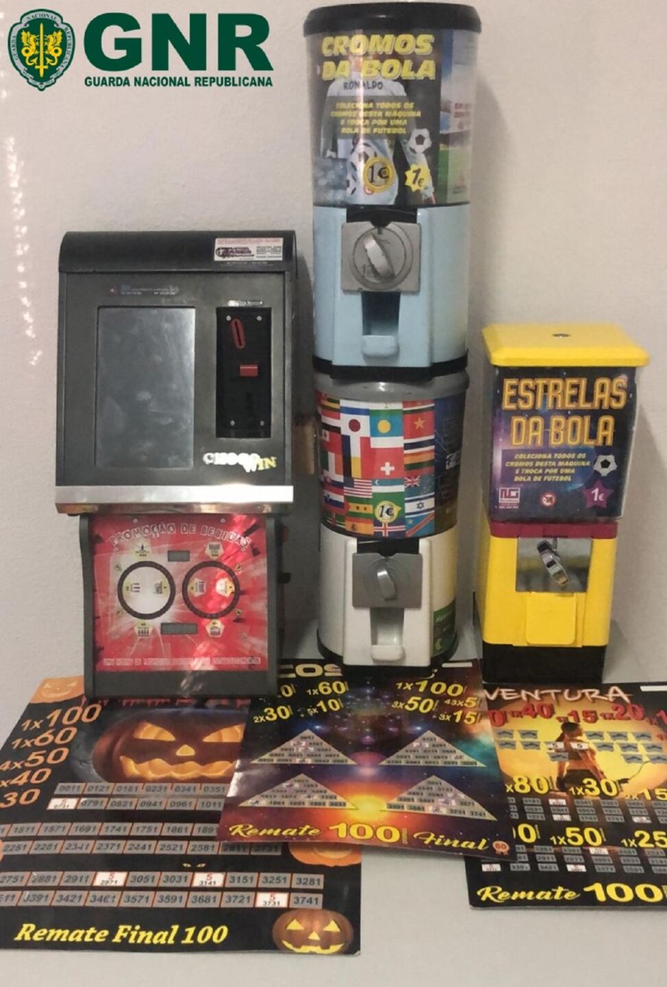 A imagem mostra máquinas de venda de cromos e outros artigos relacionados com futebol, além de cartelas numeradas com prémios. No canto superior esquerdo surge o logótipo da Guarda Nacional Republicana (GNR).