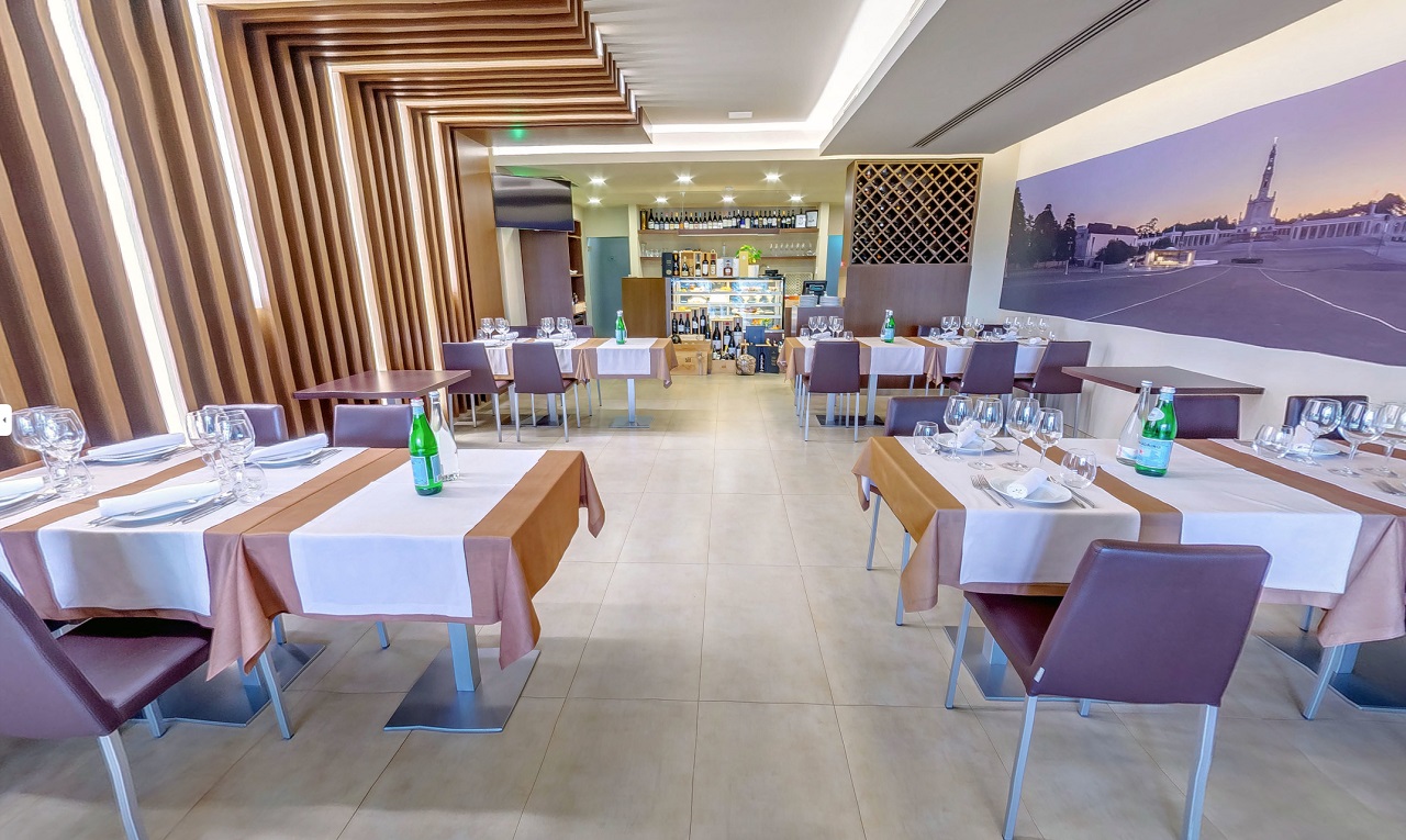 Sala de restaurante vazia, com mesas postas para refeições e um balcão ao fundo. Na parede, há uma imagem de um santuário.