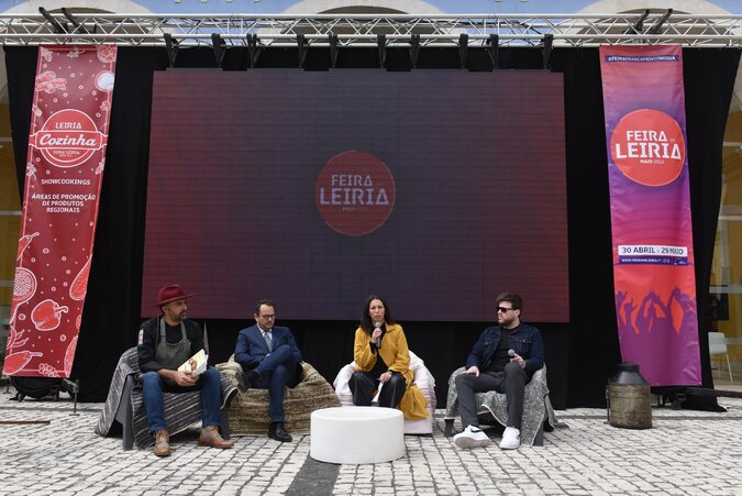 Quatro pessoas participam numa conversa em palco na Feira de Leiria; uma delas fala ao microfone. Ao fundo, um ecrã e uma faixa exibem o nome do evento.