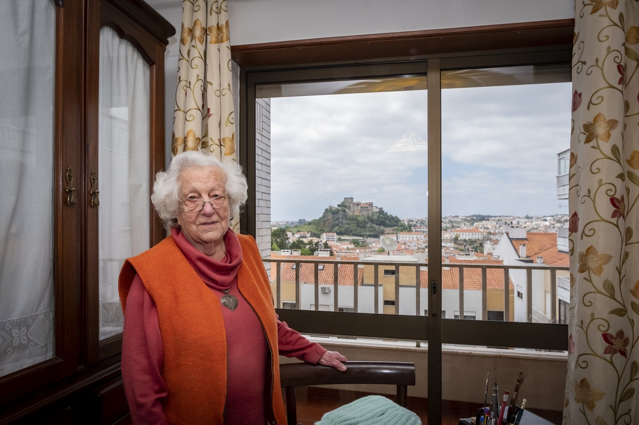 Fotografia de Antonieta Brita na sua casa com janela e o castelo em fundo
