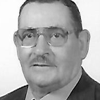 Retrato a preto e branco de um homem com óculos e bigode, vestido com fato e gravata.