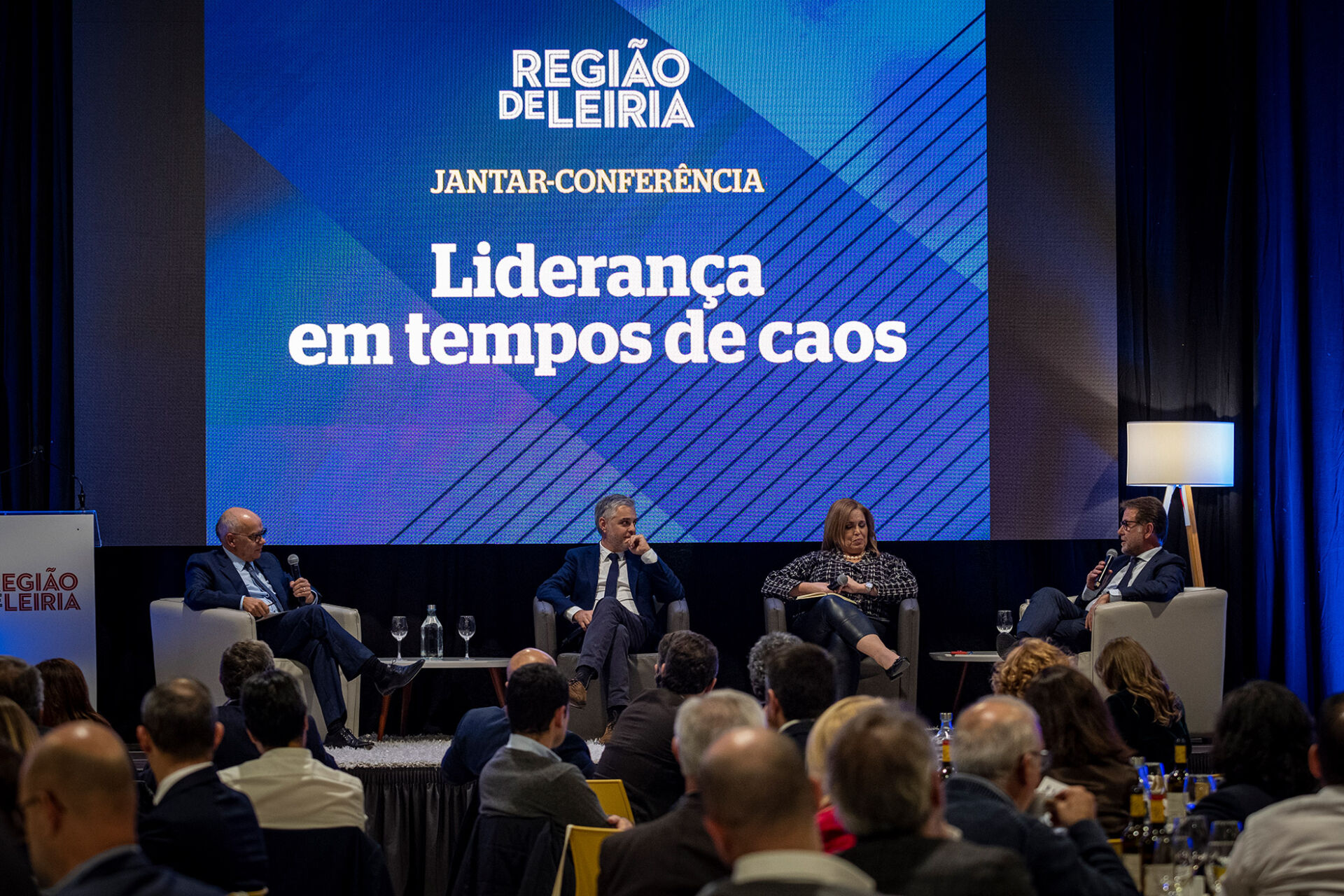 Quatro participantes estão sentados em palco perante uma plateia, num jantar-conferência da Região de Leiria. No ecrã lê-se «Liderança em tempos de caos».