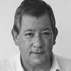 Retrato a preto e branco de um homem de meia-idade, de frente para a câmara. Veste uma camisola clara.
