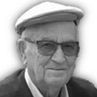 Retrato a preto e branco de um homem idoso com óculos e boné, a olhar para a câmara. Não há texto visível que permita identificá-lo.