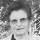 Retrato a preto e branco de uma mulher de óculos, fotografada ao ar livre. Vê-se vegetação ao fundo.