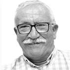 Retrato a preto e branco de um homem de cabelo branco, bigode e óculos, com uma camisola de padrão axadrezado.