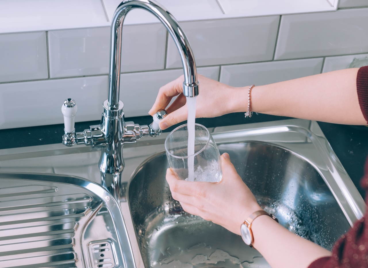 Mãos de uma mulher a encher um copo de água a partir de uma torneira na cozinha