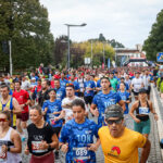 Uma multidão de participantes corre numa prova de 10 km numa avenida arborizada. Vêem-se dorsais e espectadores junto ao percurso.