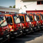 Vários veículos vermelhos dos bombeiros estão estacionados em fila junto a um edifício. Num dos veículos lê-se «Leiria».