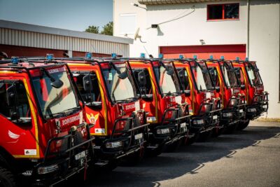 Vários veículos vermelhos dos bombeiros estão estacionados em fila junto a um edifício. Num dos veículos lê-se «Leiria».