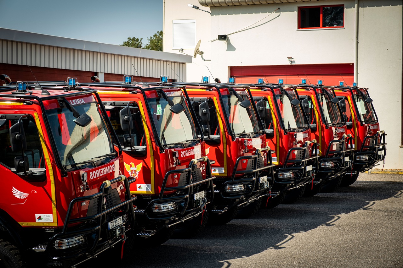 Vários veículos vermelhos dos bombeiros estão estacionados em fila junto a um edifício. Num dos veículos lê-se «Leiria».