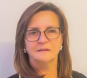 Retrato de uma mulher de óculos, com cabelo castanho e brincos de pérolas, sobre um fundo claro. Não há texto visível que permita identificá-la.
