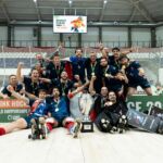 Uma equipa de hóquei em patins posa com medalhas e um troféu num pavilhão. Na imagem são visíveis referências ao Campeonato do Mundo de Hóquei em Patins e aos World Skate Games Asunción 2026.