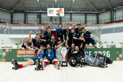 Uma equipa de hóquei em patins posa com medalhas e um troféu num pavilhão. Na imagem são visíveis referências ao Campeonato do Mundo de Hóquei em Patins e aos World Skate Games Asunción 2026.