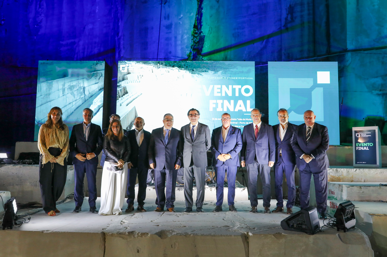 Um grupo de pessoas posa num espaço industrial, diante de painéis com a inscrição «Evento Final». A imagem mostra a referência «Sustainable Stone by Portugal».