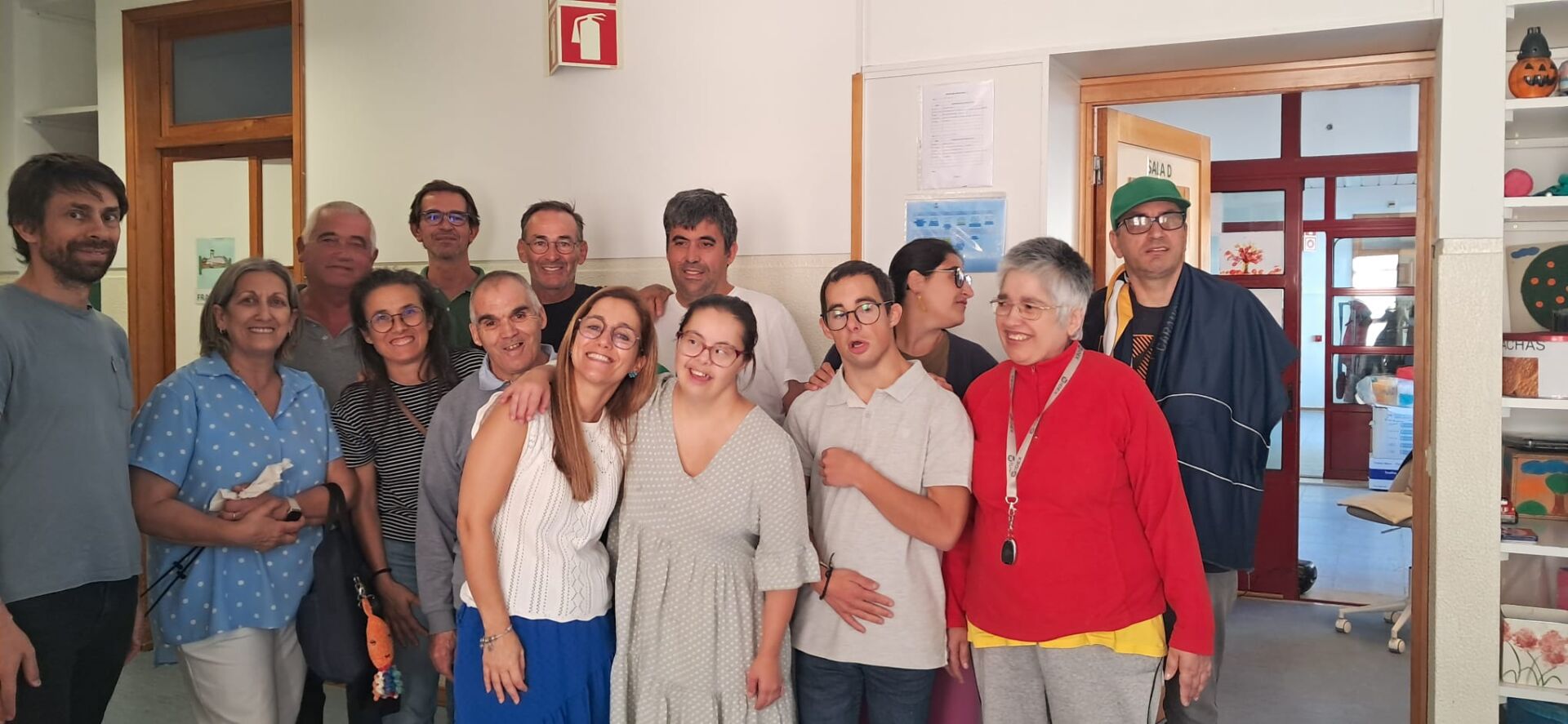 Um grupo de pessoas posa para uma fotografia no interior de um edifício. Ao fundo, vê-se uma porta aberta com a indicação «SALA D».
