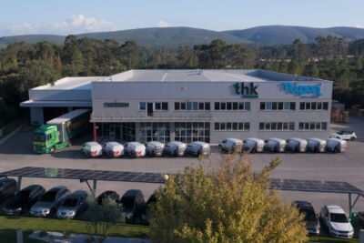 Vista aérea de um edifício industrial com os letreiros «DISTERM», «thk thinktech» e «nipon». Há carrinhas e um camião estacionados em frente, além de painéis solares sobre o parque de estacionamento.
