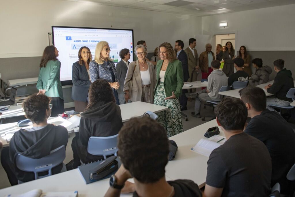 Um grupo de adultos conversa com alunos numa sala de aula. Num ecrã está projetado material sobre Alberto Caeiro.