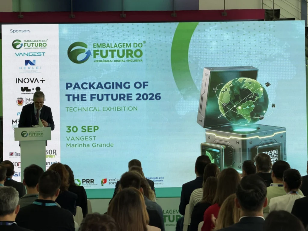 Um orador discursa perante uma plateia, junto a um ecrã que anuncia a exposição técnica «Packaging of the Future 2026», em 30 de setembro, na Vangest, Marinha Grande. São visíveis os logótipos de várias entidades patrocinadoras.