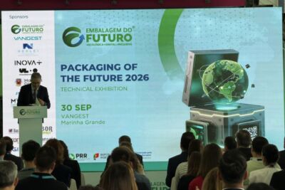 Um orador discursa perante uma plateia, junto a um ecrã que anuncia a exposição técnica «Packaging of the Future 2026», em 30 de setembro, na Vangest, Marinha Grande. São visíveis os logótipos de várias entidades patrocinadoras.
