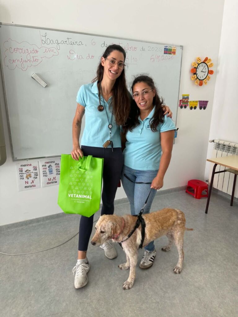 Duas mulheres posam com um cão com trela numa sala com um quadro branco. Uma delas segura um saco verde com a inscrição «VETANIMAL».