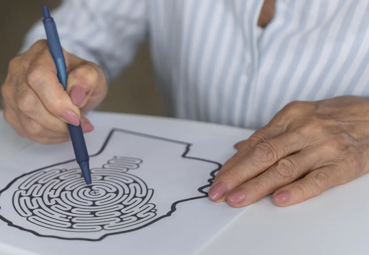 Uma pessoa segura uma caneta sobre uma folha com um labirinto impresso, enquanto apoia a outra mão no papel. O rosto não está visível.