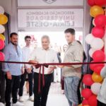 Um homem prepara-se para cortar uma fita numa cerimónia à entrada de um espaço decorado com balões vermelhos, brancos e dourados. Na porta lê-se, de forma invertida, «Associação Académica Universidade Leiria • Oeste».