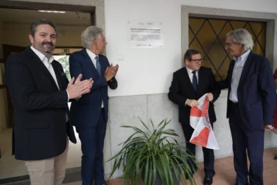 Quatro homens junto a uma placa de um centro tecnológico especializado; dois aplaudem, enquanto outro segura uma bandeira. A imagem sugere uma cerimónia de inauguração, mas a placa não permite confirmar a data nem os participantes.