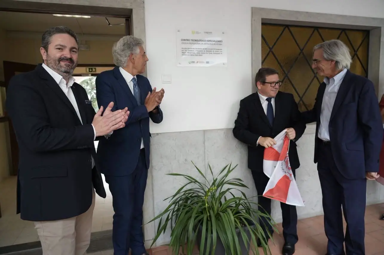 Quatro homens junto a uma placa de um centro tecnológico especializado; dois aplaudem, enquanto outro segura uma bandeira. A imagem sugere uma cerimónia de inauguração, mas a placa não permite confirmar a data nem os participantes.