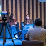 Duas mulheres participam numa conversa perante o público, com microfones e um computador portátil. Um ecrã apresenta um cartaz do HA HA Art Film Festival.