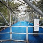 Um portão fechado impede o acesso a um parque infantil com piso azul e estrutura de rede. A placa à entrada identifica-o como «Parque Infantil Ponte», em Leiria.