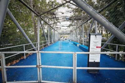Um portão fechado impede o acesso a um parque infantil com piso azul e estrutura de rede. A placa à entrada identifica-o como «Parque Infantil Ponte», em Leiria.