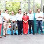 Sete pessoas estão reunidas para uma fotografia de grupo num espaço envidraçado. Ao fundo, veem-se painéis turquesa com texto parcialmente visível.