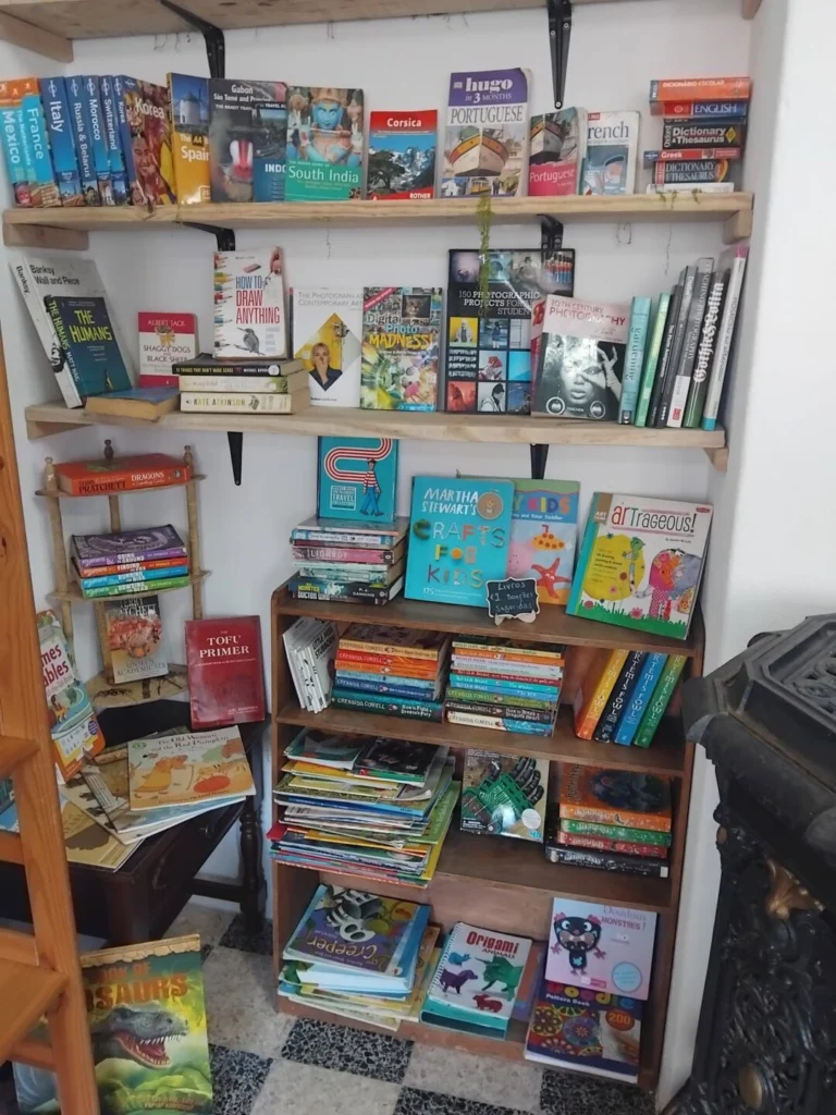 Estantes de uma livraria com livros de viagens, fotografia, arte e literatura infantil. Vê-se uma pequena placa a indicar livros a 1, 2 e 5 euros.