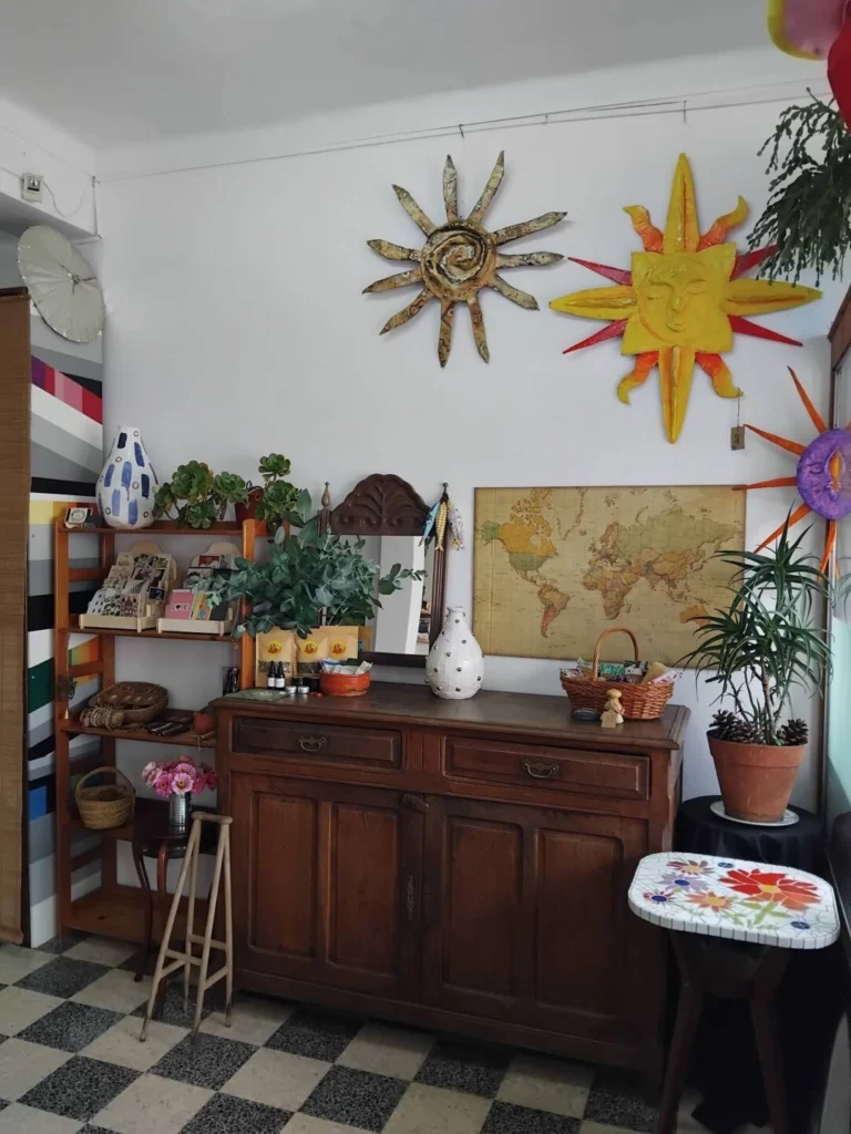 Interior com um aparador de madeira, plantas, peças decorativas e um mapa-múndi na parede. Destacam-se duas esculturas em forma de sol e um pequeno tampo com mosaico floral.